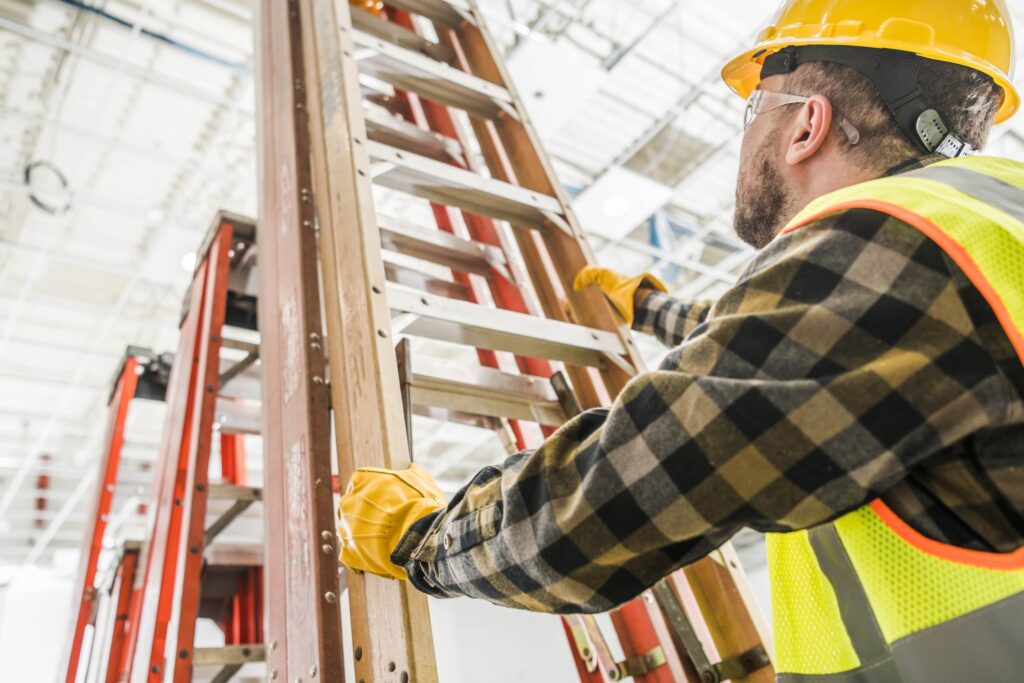 Worker on ladder against building wall, applying ladder safety tips and practicing proper fall prevention techniques.