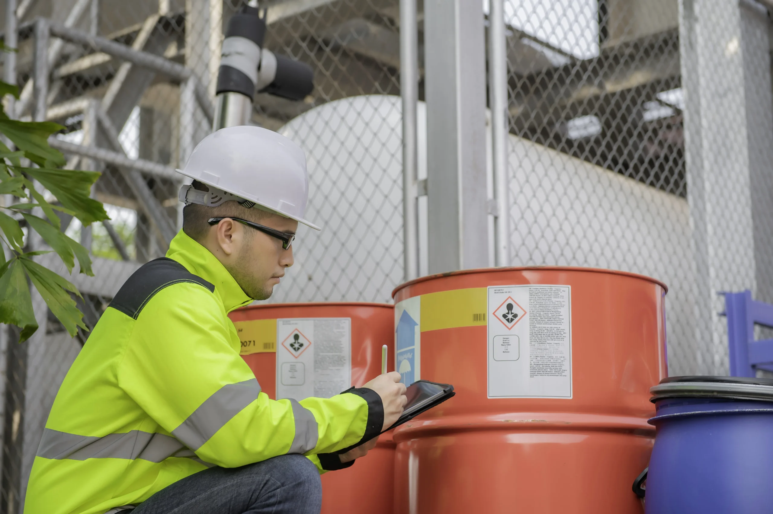 Worker inspecting hazardous chemical barrels with proper labeling under WHMIS 2025 compliance.
