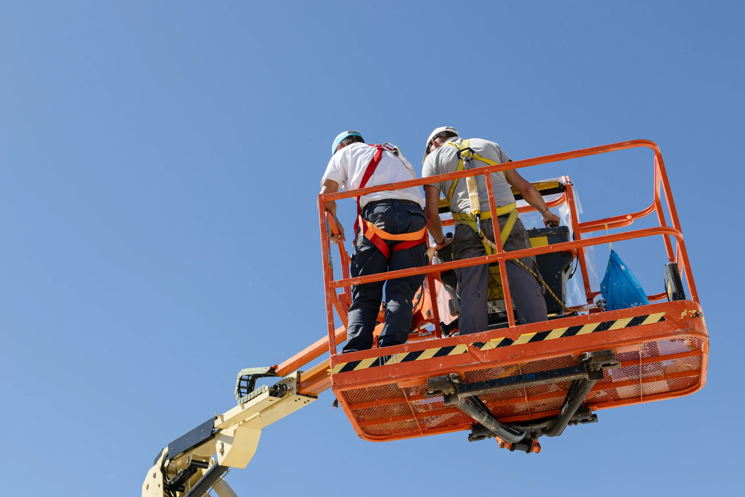 Worker operating an aerial lift wearing fall protection harness to ensure aerial lift safety compliance